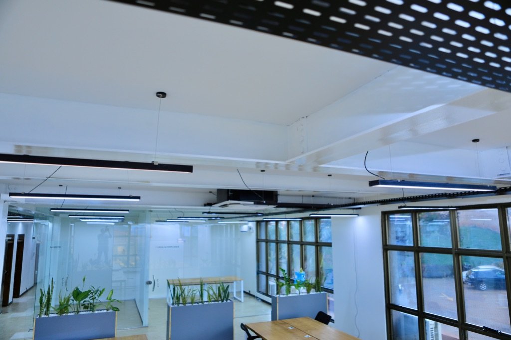Exposed ceiling with perforated cable tray, LED strips, and glass partition offices